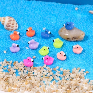 Miniature resin ducks in various colors on blue sand and pebble beach landscape