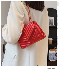 Detail of red patent leather chain bag with V-shaped quilting and gold metal strap