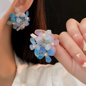 Gros plan sur boucles d'oreilles fleurs en acrylique bleu avec perle sur la main