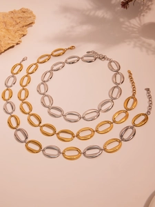 Close-up of chunky gold and silver oval link chains on a neutral textured stone