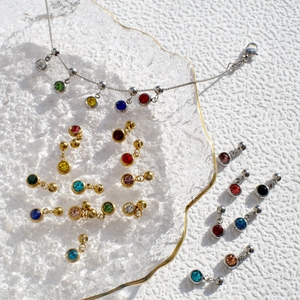 Silver stainless steel birthstone necklace with colorful gem charms on a glass tray