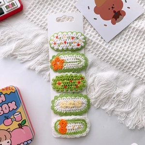 Detailed view of handmade knitted flower and fruit hair clips on white card holder