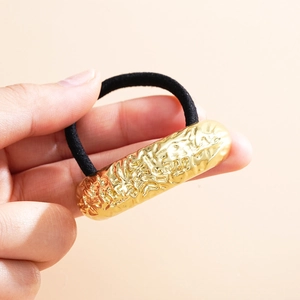 Close-up of a black elastic hair tie with a hammered gold metal decorative accent