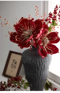 Close-up of velvet red Christmas flowers with gold glitter and red beads in stone vase