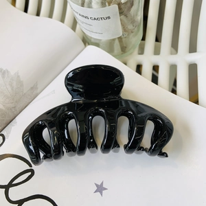 Detail of a large glossy black flower hair claw clip on white book pages background