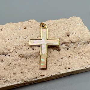 Macro shot of gold cross pendant with iridescent shell inlay on a textured stone base