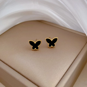 Detailed view of butterfly stud earrings with black inlay and golden beaded milgrain edges
