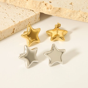 Pair of gold and silver stainless steel star stud earrings on a textured stone base