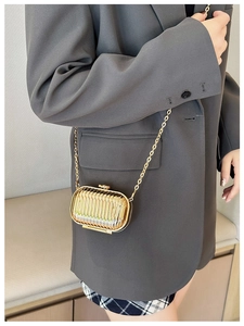 Detail of gold oval mini chain bag with vertical wave texture on a grey blazer suit