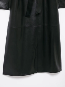 Detail shot of black long leather coat featuring matching waist belt and subtle sheen