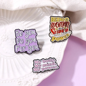 Enamel heart lapel pins with inspirational text displayed on a white textured ceramic dish