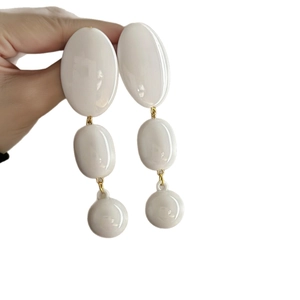 White acrylic oval tassel earrings with golden metal links held against plain background