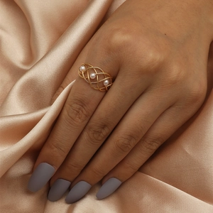 Macro shot of gold hollow woven ring with white pearls on luxury champagne silk