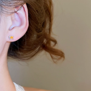 Gros plan d'une mini boucle d'oreille étoile en émail orange portée sur le lobe de l'oreille