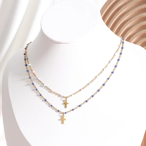 Detail of double-layered gold necklace featuring colorful beads and cross pendants on a model