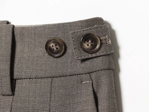 Detailed close-up of side waist adjusters with textured buttons on brown dress pants