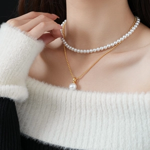 Detail of layered gold-plated necklace with faux pearls worn by a model on a dark sweater