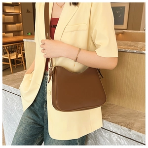 Gros plan d'un sac hobo minimaliste en cuir marron porté avec un blazer décontracté