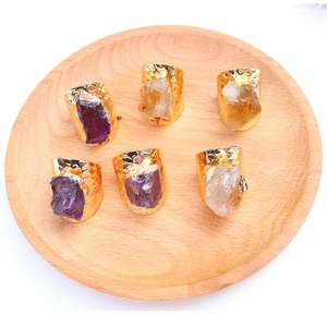 Detailed top view of six bohemian raw amethyst and crystal gold rings on a wooden tray