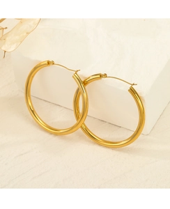 Detailed close-up of thick gold-plated stainless steel hoop earrings on a marble stone surface
