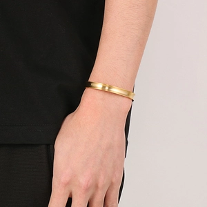 Close-up of a minimalist golden stainless steel open bangle worn on a model's wrist