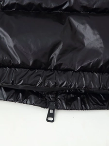 Detail of glossy black puffer vest showing hem stitching and metallic zipper closure