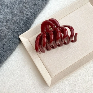 Macro shot of glossy deep red hair claw clip on beige textured fabric display