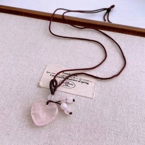 Macro detail of a heart-shaped rose quartz pendant on a brown woven necklace rope