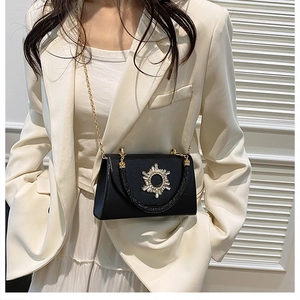 Detail of black leather crossbody bag with golden rhinestone sunburst decor on a model