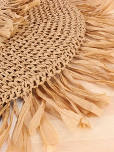 Bohemian style round straw woven placemat with fringe details on wood table