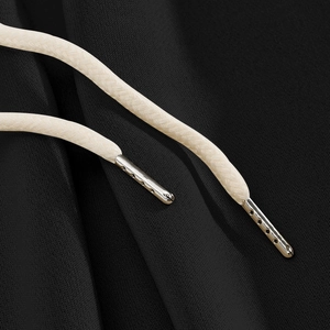 Detail of beige woven drawstring with silver metal tips on black knit casual trousers