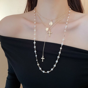 Close-up of layered gold necklaces with cross pendants and pearls on a model