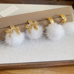 Elegant gold flower zircon earrings with white fur balls on a beige jewelry display stand