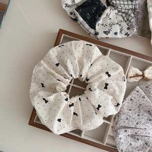 Close-up of a large cream cotton scrunchie with black polka dots and bows in a wood tray