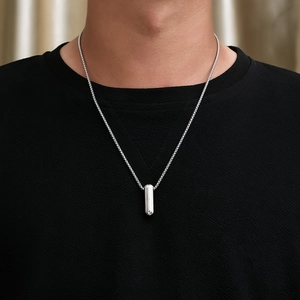 Gros plan d'un collier pendentif capsule argenté pour homme avec textures verticales