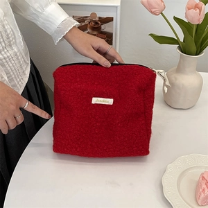 Handheld weergave van een rode teddy fleece make-uptas met een minimalistisch label