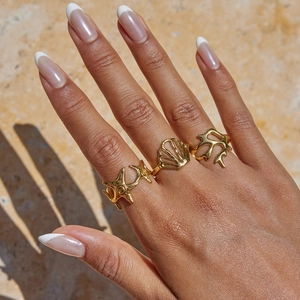 Detailed view of ocean-themed gold starfish, shell, and coral rings set on a model hand