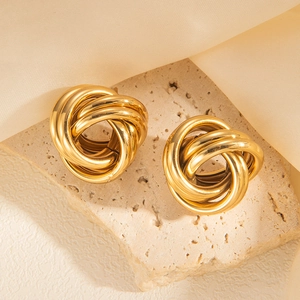 Close-up of golden geometric knotted hoop earrings on a natural beige stone pedestal