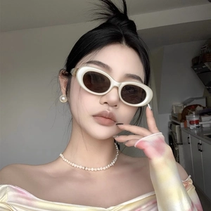 Close-up of milky white oval frame sunglasses worn by model with pearl accessories