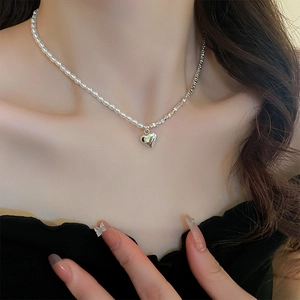 Detail of a layered necklace with silver metal links, white pearls, and a heart pendant