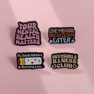 Close-up of four colorful enamel mental health quote pins on a pinkish background