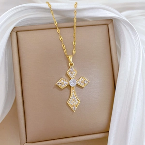 Close-up of gold-plated titanium cross pendant with clear cubic zirconia in beige jewelry box