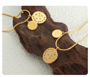 Close-up of gold snake chain necklace with Good Luck engraved disk and zircon pendant