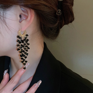 Close-up of black geometric crystal tassel earrings on model with golden metal accents