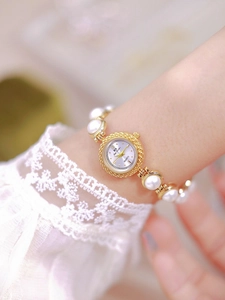 Detail of luxury white dial gold watch with elegant pearl bracelet on female wrist