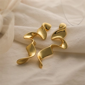 Nahaufnahme goldener Ohrringe im Wellendesign auf weichem Stoff mit skulpturalem Detail