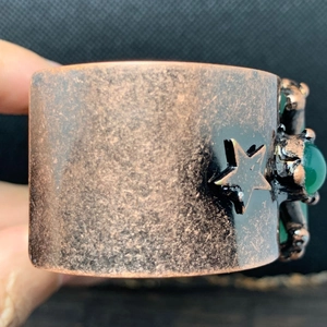 Makroaufnahme von Bronze-Armreif mit Sternmustern und eingelegtem grünen Edelstein