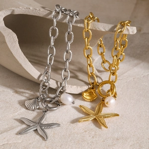 Macro detail of 18k gold starfish shell and pearl ocean charms on linked chain