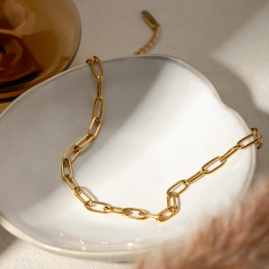 Close-up of 18K gold-plated paperclip chain necklace on an aesthetic white ceramic tray