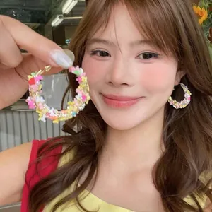 Close-up of hand-woven colorful flower and butterfly hoop earrings worn by a model